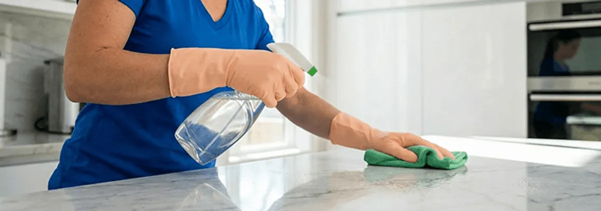 Maid service worker spraying and wiping a kitchen countertop with a microfiber cloth for sanitizing, Columbia, MO.